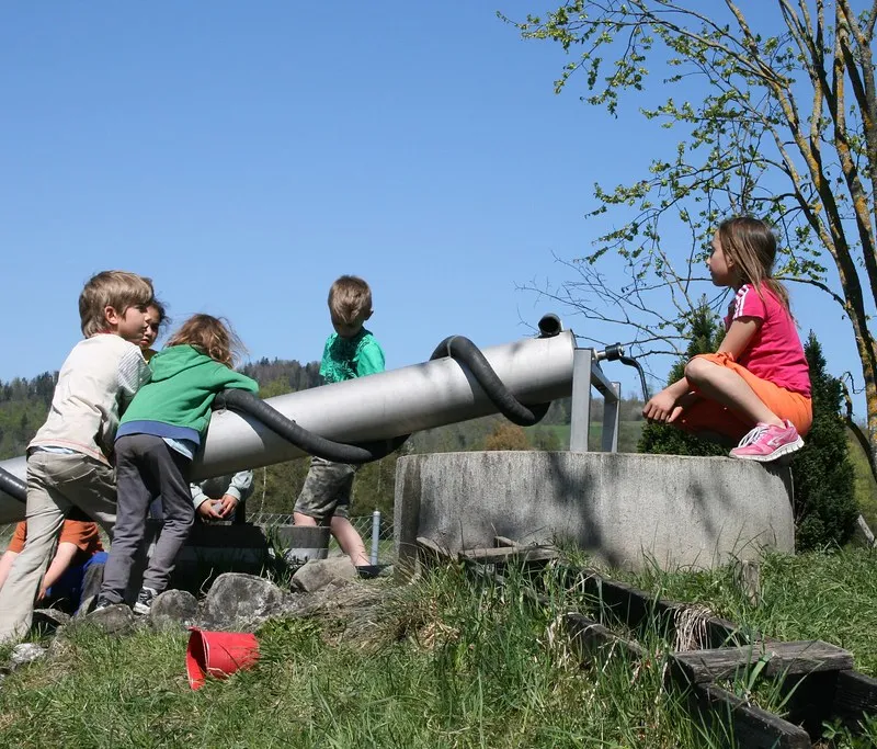 Kinder erkunden eine grosse Spielanlage mit Rohr und Rutsche.