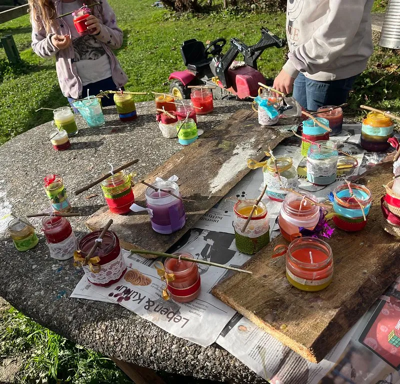 Kinder gestalten bunte Windlichter an einem Tisch im Freien.